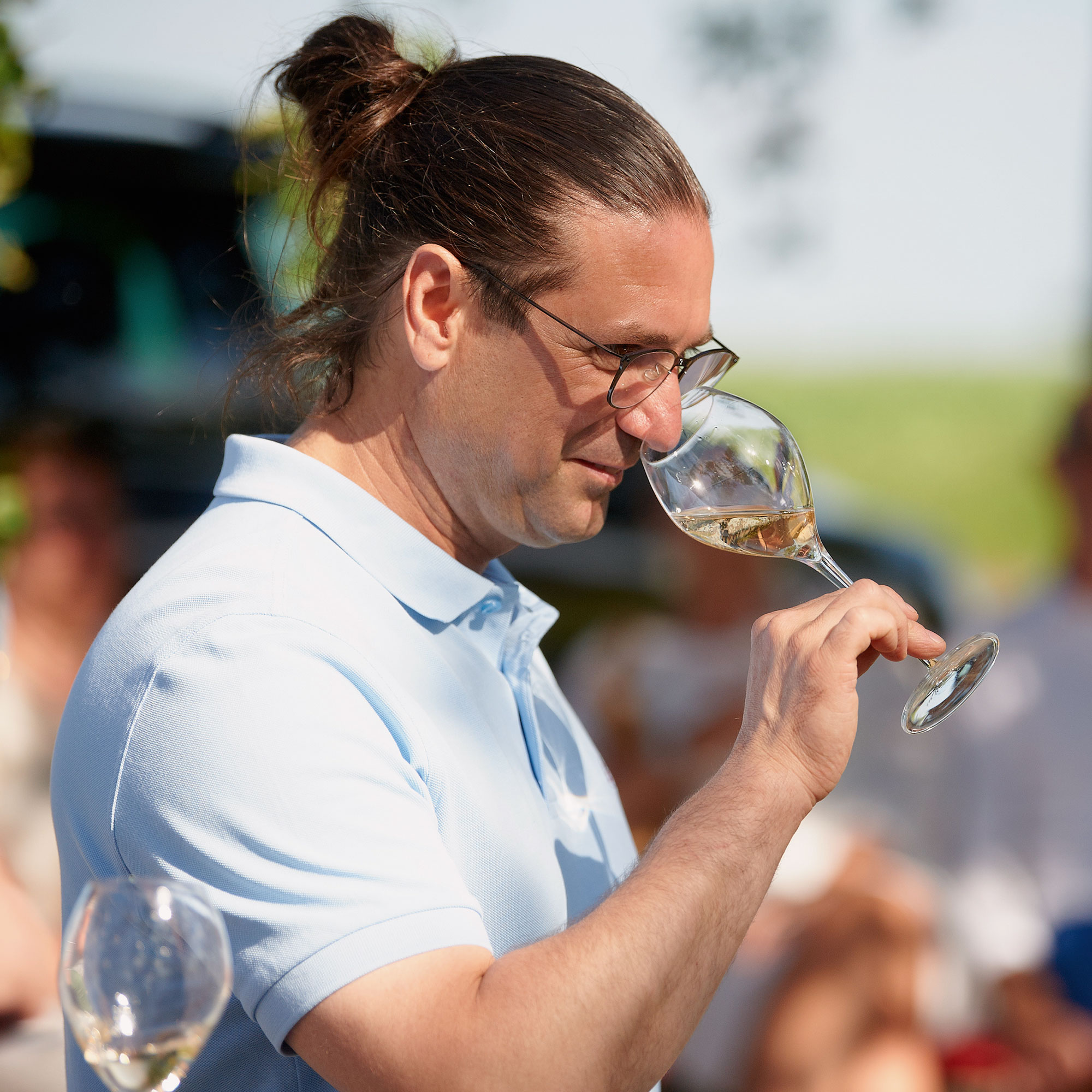 Mann mit Zopf und hellblauem Polohemd verkostet Apfelwein im Glas auf dem Obsthof am Steinberg