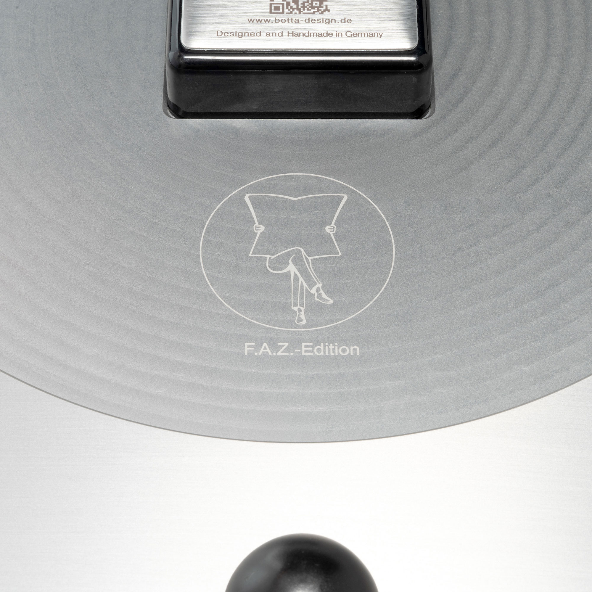 Graviertes FAZ-Edition-Logo mit lesender Figur auf silberner Rückseite der UNO 24 Aerolith Wanduhr von BOTTA