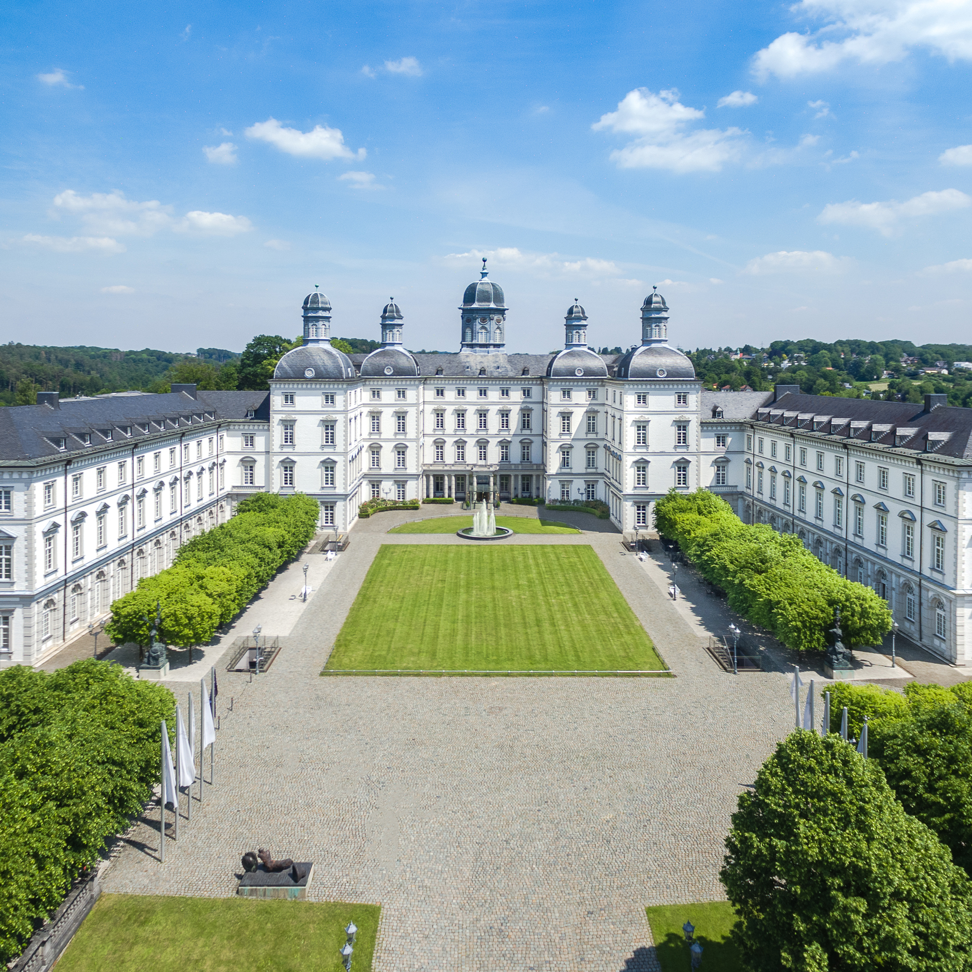 Barockes Schloss Bensberg mit symmetrischem Innenhof, Brunnen und gepflegter Rasenfläche unter blauem Himmel