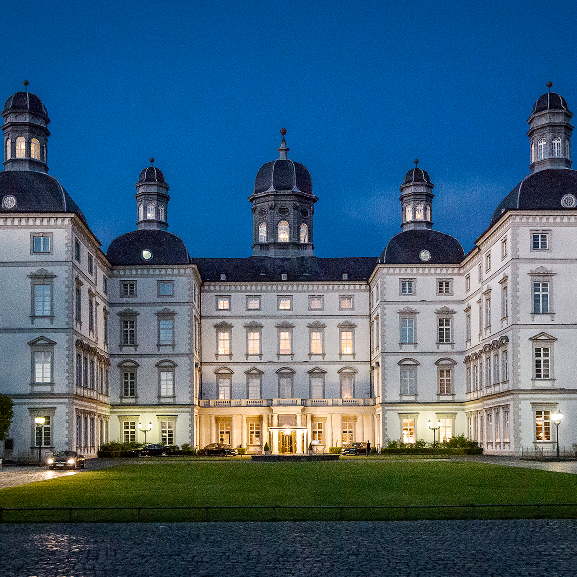 Beleuchtete Fassade von Schloss Bensberg bei Nacht, symmetrische Architektur und gepflegter Vorplatz