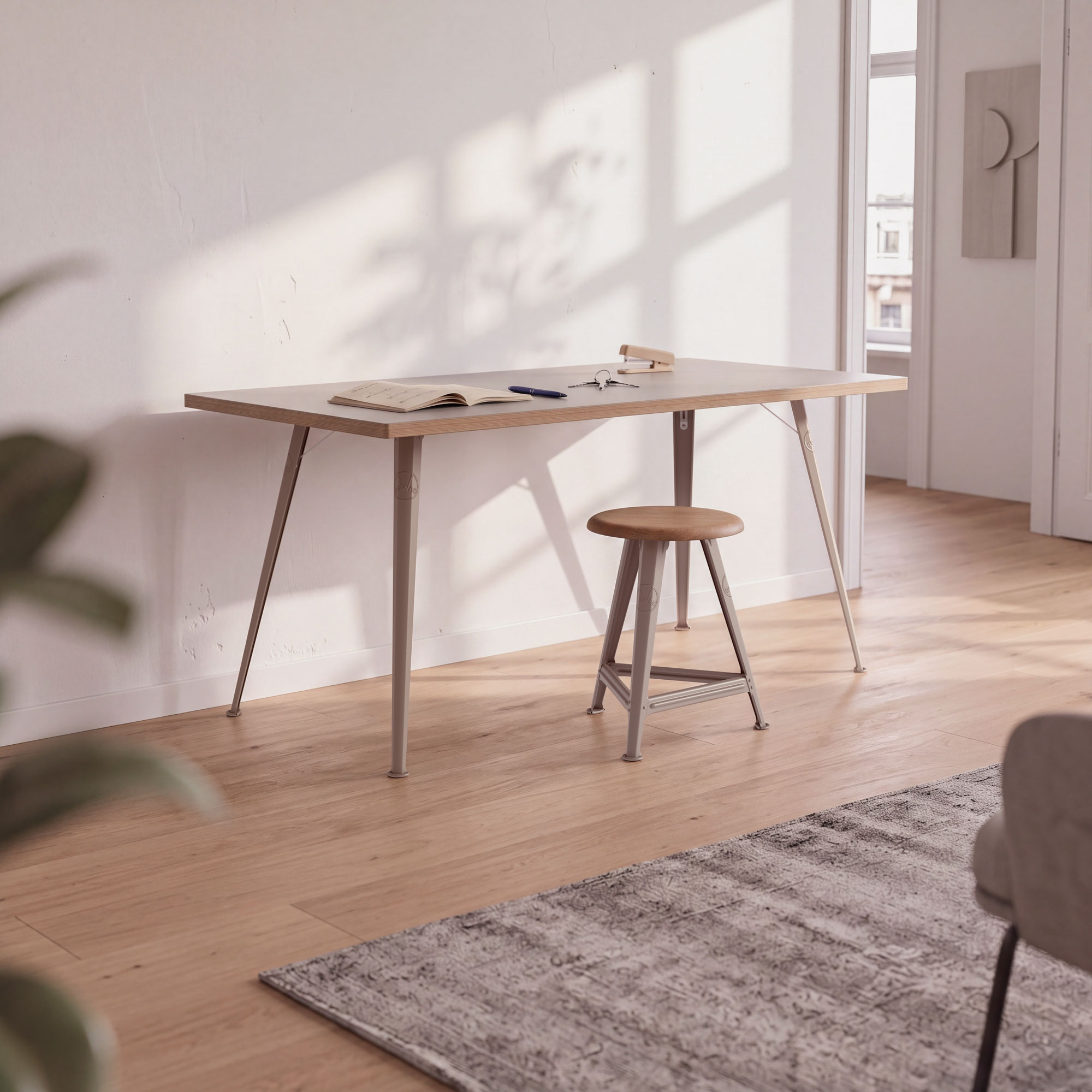 Rowac-Tisch in Sonderfarbe Desert Sand mit Stahlgestell, aufgestellt in heller Wohnung, daneben passender Hocker